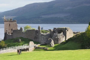 Urquhart Castle ruins beside Loch Ness with visitors on grassy shore