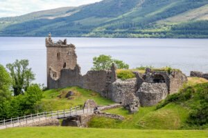 Ruined tower of Urquhart Castle beside Loch Ness and grassy banks