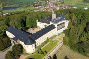 Aerial view of Zbiroh Castle surrounded by forest, gardens, and nearby village