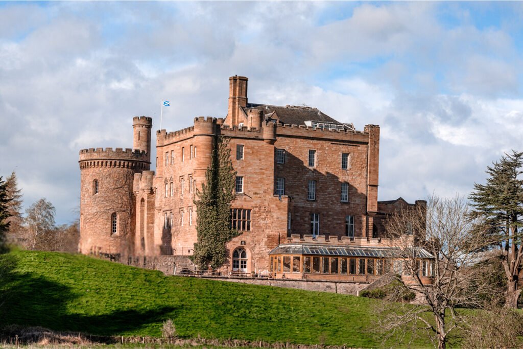 Dalhousie Castle on grassy hill under cloudy sky