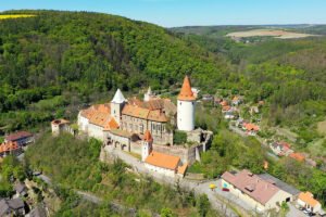 Aerial view of Krivoklat Castle atop wooded hill with tower and red roofs