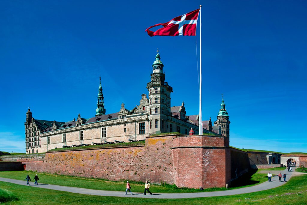 Kronborg Castle from grassy approach with Danish flag and visitors under blue sky