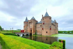Muiderslot Castle reflected in moat with green lawns and cloudy sky