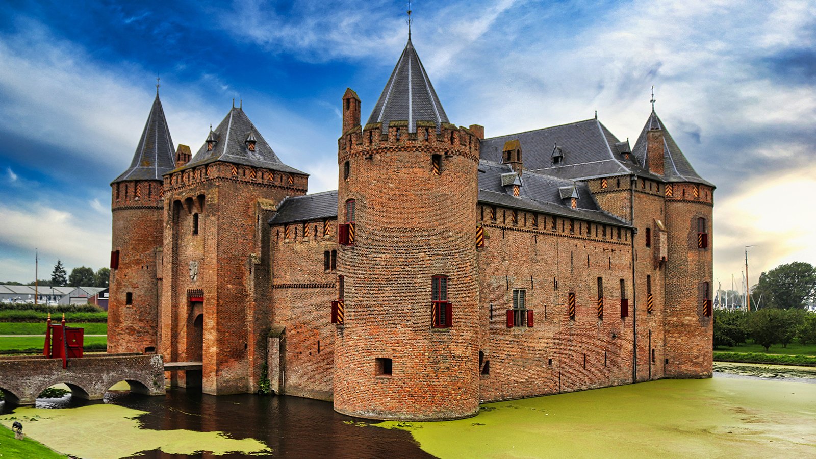 Muiderslot Castle across green moat under dramatic cloudy sky