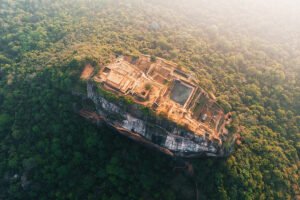Aerial view of Sigiriya rock fortress perched above jungle, showing ruins and pools