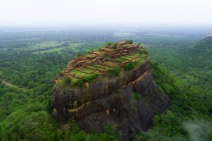 Aerial view of Sigiriya rock fortress perched above lush green Sri Lankan forest