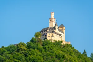 Marksburg Castle perched atop wooded hill against clear blue sky