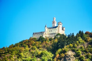 Marksburg Castle perched on forested hill under clear blue sky