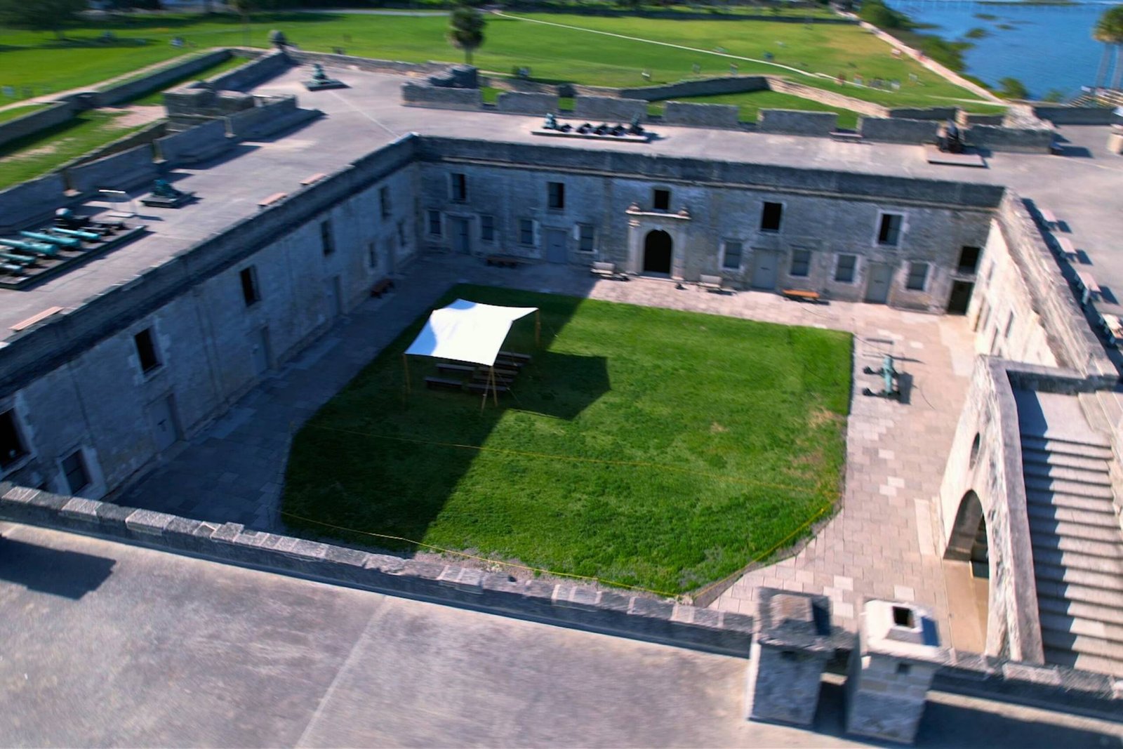 Interior courtyard of Castillo de San Marcos in St. Augustine, Florida, showing historic stone walls, arched entryways, cannons, and a canopy over the grassy center.