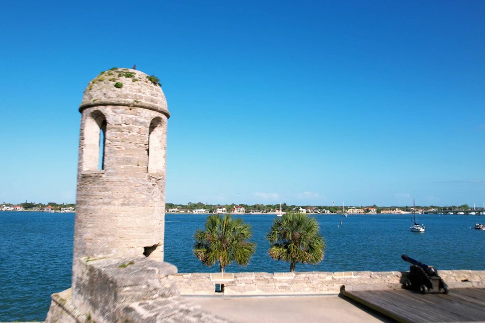 Watchtower and cannon at Castillo de San Marcos overlooking Matanzas Bay in St. Augustine, Florida, with sailboats and palm trees in the background.