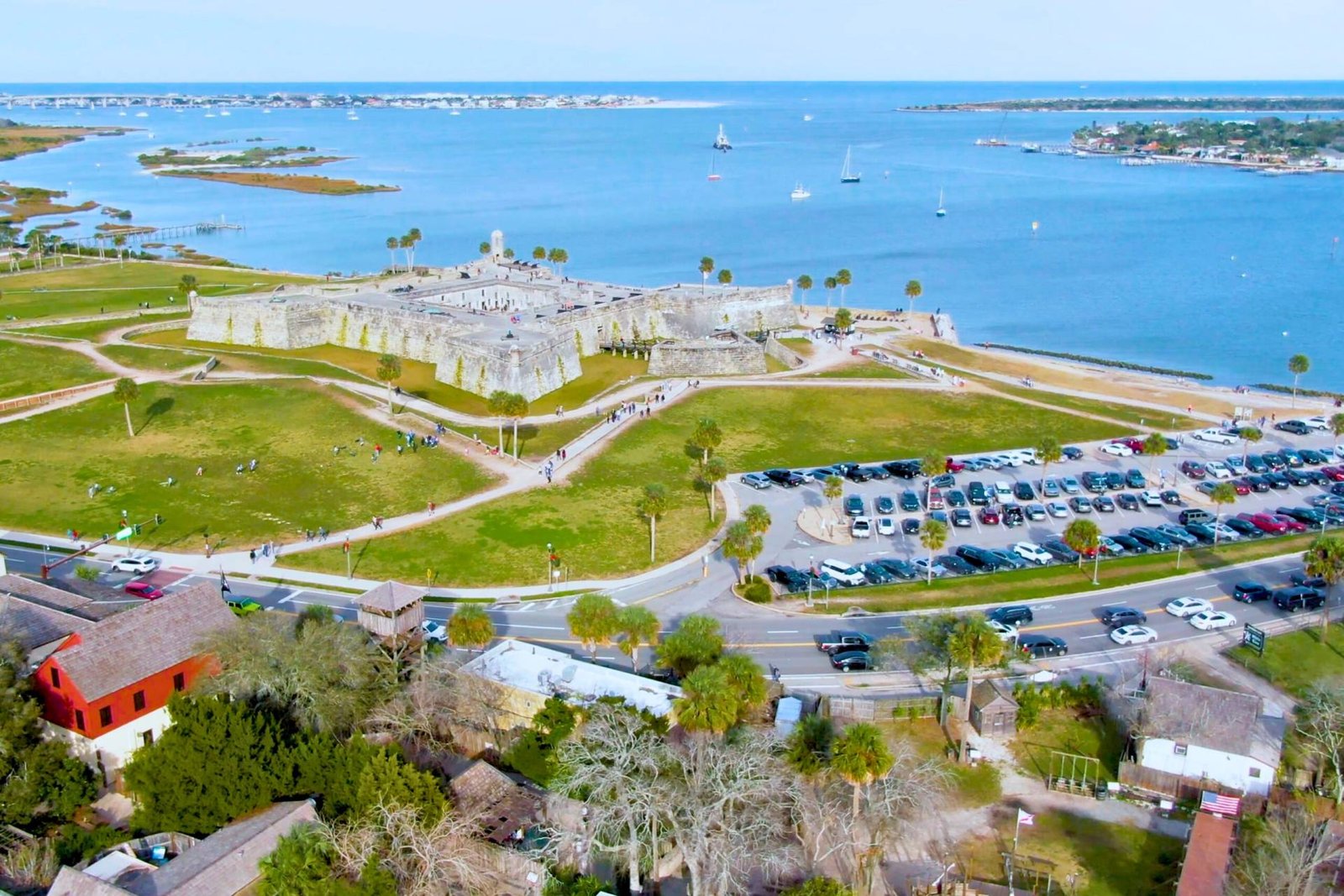 Wide aerial view of Castillo de San Marcos in St. Augustine, Florida, showing the fortress, parking area, nearby streets, and scenic coastline along Matanzas Bay.